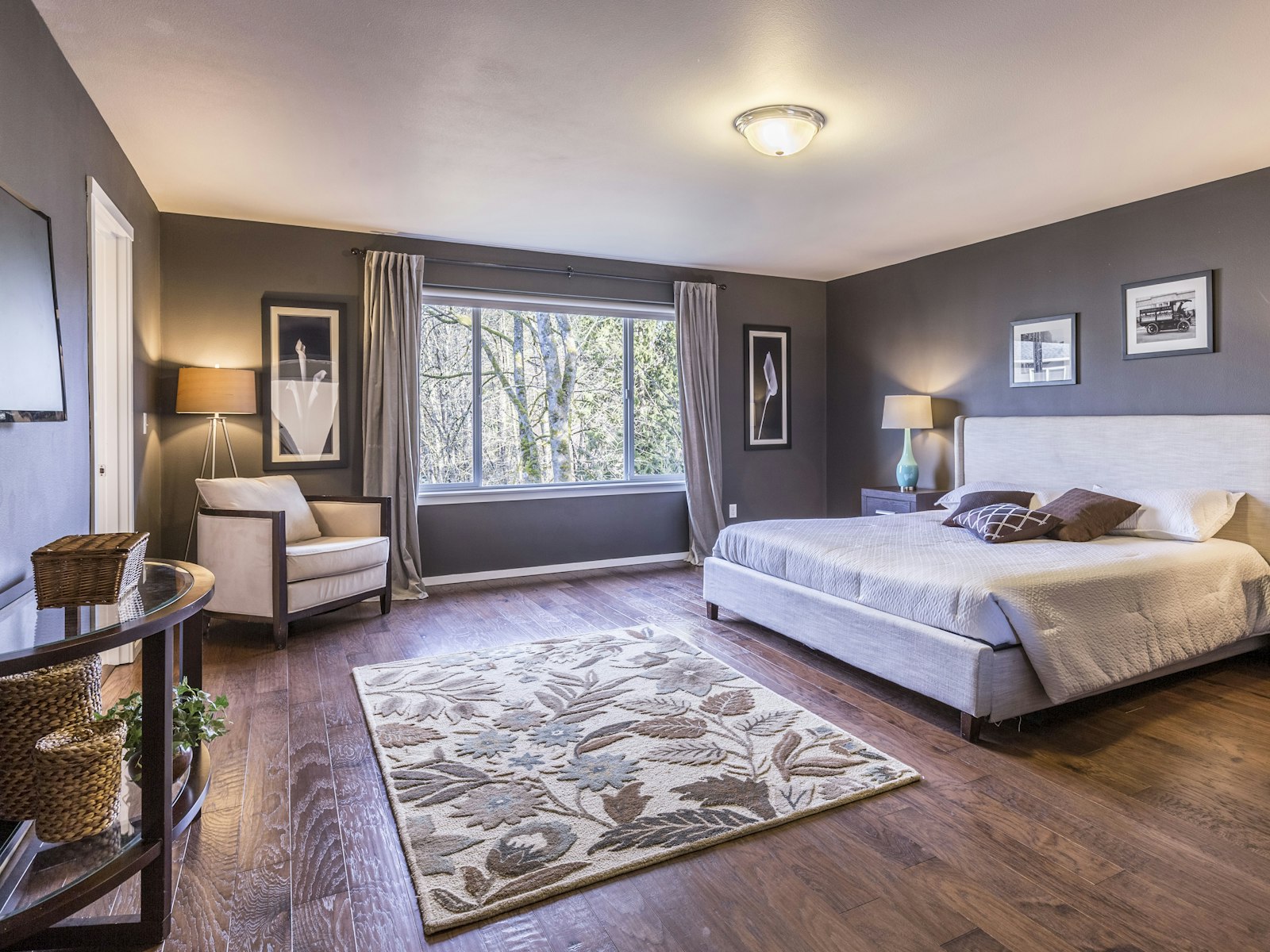 Bedroom with dark grey walls, a large bed, an armchair by the window and a floral area rug