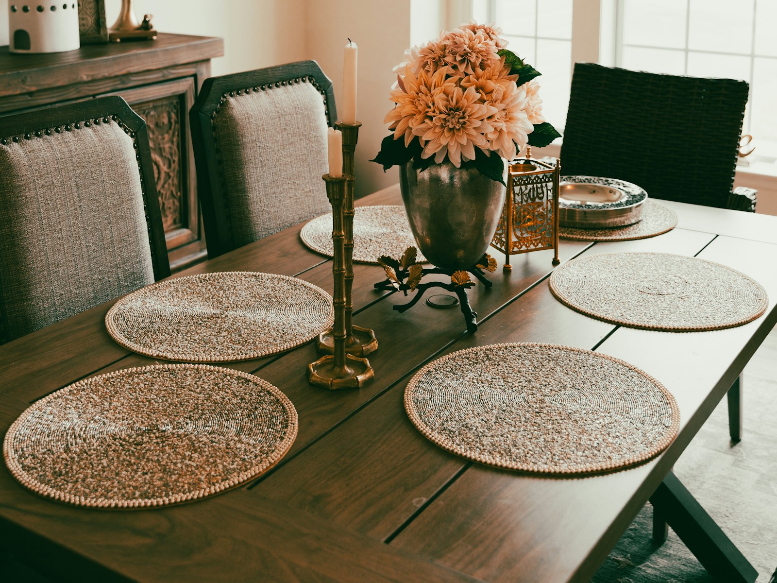 Dining table set with woven placemats, brass candlesticks and peach flowers