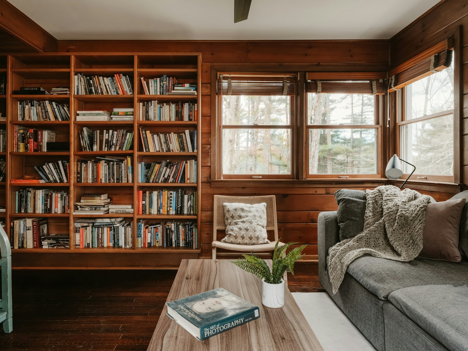 Wood-panelled library with full bookshelves, a grey sofa and a window seat